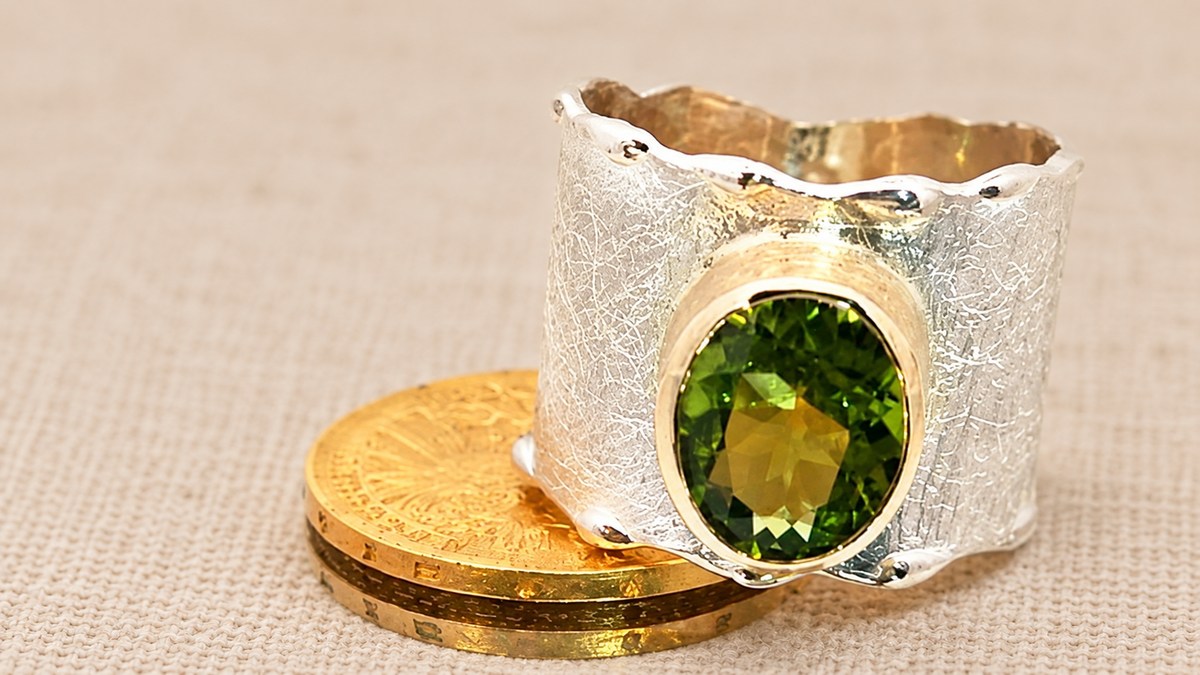 Autorinis sidabro žiedas su aukse įtvirtintu olivinu (peridotu) ant šilto lino fono – SAVA juvelyrika.